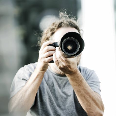 Das Aufnahme zeigt eine männliche Person, die ein Foto mit einer Spiegelreflexkamera macht.