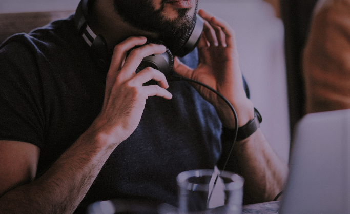 Das Bild zeigt eine Person, die an einem Schreibtisch sitzt. Die Person trägt Kopfhörer um den Hals. (Quelle: Canva) Das Bild zeigt eine Person, die an einem Schreibtisch sitzt. Die Person trägt Kopfhörer um den Hals.