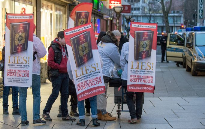 Die Aufnahme zeigt Personen mit Transparenten zur "Lies!"-Kampagne. (Quelle: Picture Alliance/dpa/Boris Roessler) Die Aufnahme zeigt Personen mit Transparenten zur "Lies!"-Kampagne.
